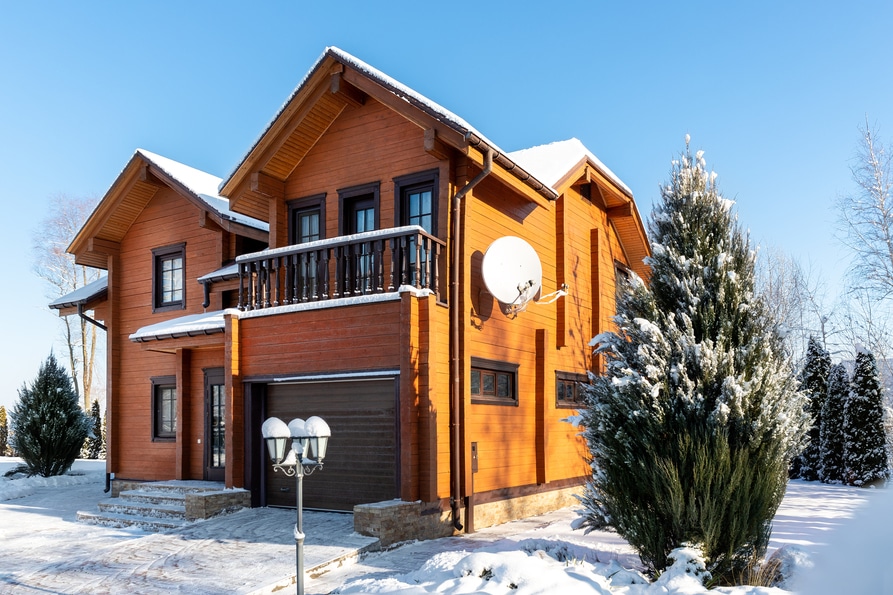 scenery facade front view of modern wooden luxury timber eco house villa with garage door snowcapped by white fresh snow at cold sunny winter day. real estate building construction project exterior