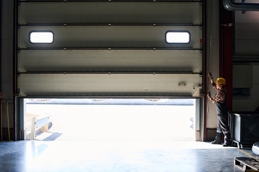 young female worker of factory or hangar opening shutter roller door