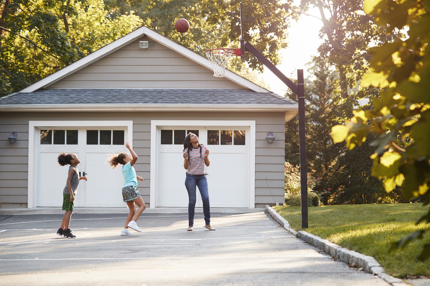 mother and children playing basketball on driveway at home